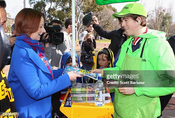 Australian Prime Minister Julia Gillard buys a copy of the AFL Record as she makes her way to an Australian Rules football game after launching the...