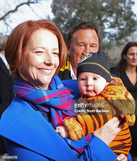Australian Prime Minister Julia Gillard is watched by her partner Tim Mathieson as she holds a baby dressed in the colours of the Richmond Tigers as...
