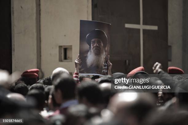 An Egyptian Christian Copt holds a portrait of late Pope Shenuda III as mourners wait in a queue to enter Saint Mark's Coptic Cathedral in Cairo's...