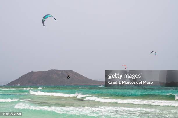 Man is seen flying while kite surfing with Lobos Island in the background during a summer day at the crystal clear turquoise waters of Corralejo...