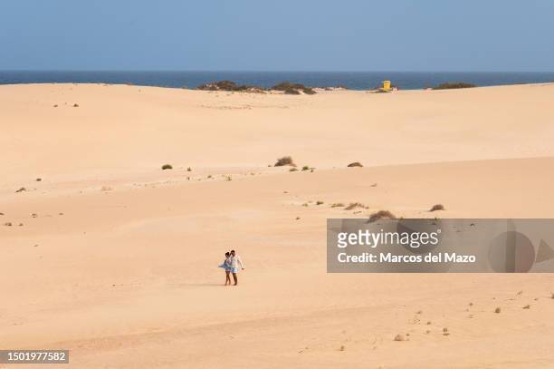 Couple of tourists walk along the sand during a hot summer day at the Dunes of Corralejo, north of Fuerteventura in the Canary Islands. The Corralejo...