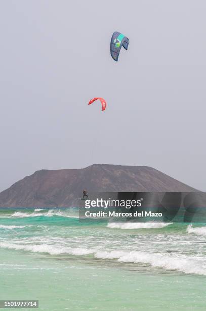 Man is seen flying while kite surfing with Lobos Island in the background during a summer day at the crystal clear turquoise waters of Corralejo...