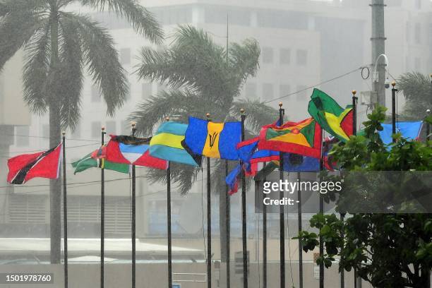 Flags of various CARICOM nations flutter in the pouring rain at the entrance of the Hyatt Regency Hotel in Port of Spain on July 4 in the framework...