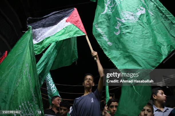 Palestinian raises the national flag as Hamas supporters wave green Islamic flags during a solidarity demonstration protesting the storming of Jenin...