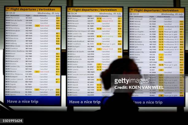 Woman stands in front of flight information boards at Schiphol Airport, near Amsterdam, July 5, 2023. Strong wind and poor visibility caused by rain...