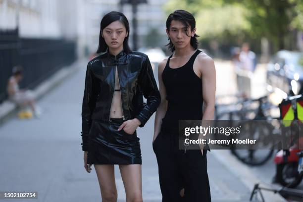 Two Fashion Week guest are seen wearing complete black outfits with a black shiny mini skirt and matching cropped shiny jacket, black bra and black...