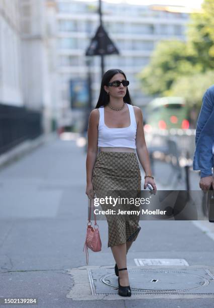 Fashion Week guest is seen wearing a white tank top, Prada black shades, Gucci x Adidas beige monogram midi skirt, black heels and rose leather...