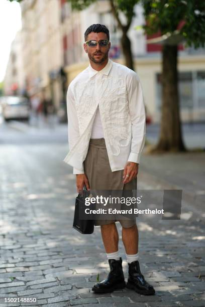 Guest wears silver sunglasses, a white with embroidered ruffled pattern shirt, a white ribbed tank-top, khaki wrap flowing knees shorts, white socks,...