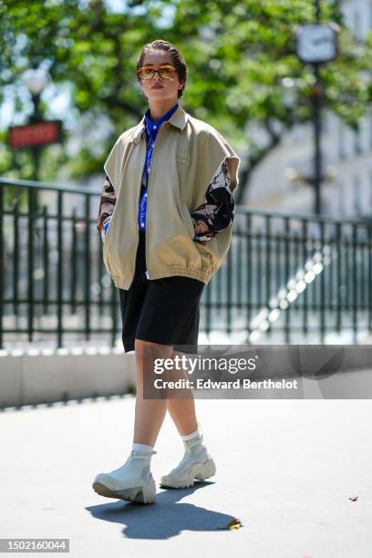 Guest wears orange glasses, a brown / black / beige print pattern with royal blue collar shirt, black suit pants, white matte leather ankle shoes ,...