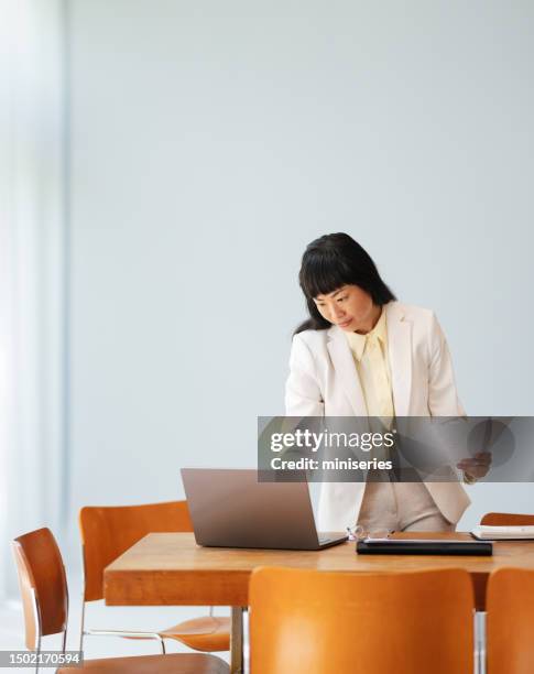 beautiful asian woman holding a piece of paper and using laptop at work - holding laptop stock pictures, royalty-free photos & images