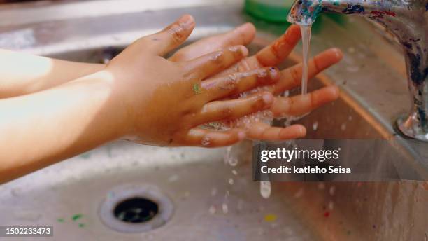 art, closeup and child washing hands with water after creative education for hygiene in a basin. health, painting and a kid with soap and liquid after a creativity class with paint at school - child washing hands stockfoto's en -beelden