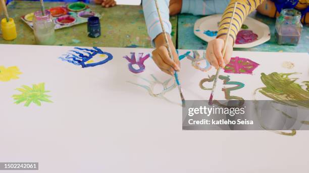 closeup hands, school kids and paintbrush in classroom, together and learning for childhood development. children students, education and academy for painting, art and color for creativity at desk - kids arts and crafts stock pictures, royalty-free photos & images