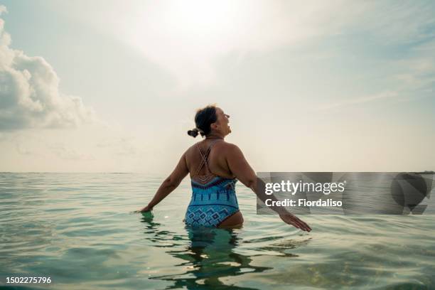 middle age woman standing in the ocean - badkleding stockfoto's en -beelden