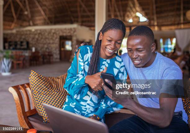 two black friends having fun sitting at home and looking at a cell phone - east africa stock pictures, royalty-free photos & images