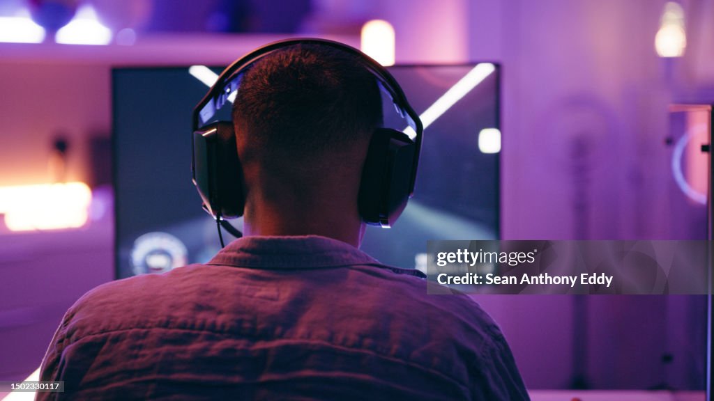 Neon, gaming and back of man with pc for live streaming esports, video games and virtual competition. Desk, computer and male gamer with headphones for playing cyber, rpg and online game on screen