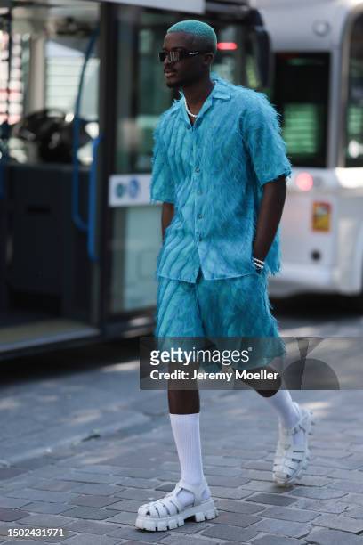 Fashion Week guest is seen wearing black balenciaga shades and a blue outfit including light blue shorts and a shirt with feathers, white socks and...