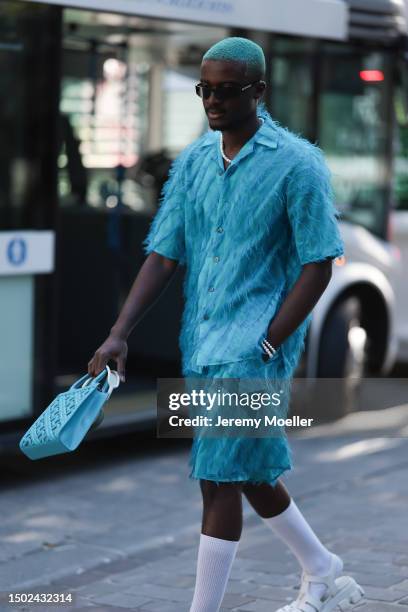 Fashion Week guest is seen wearing black balenciaga shades and a blue outfit including light blue shorts and a shirt with feathers, white socks and...