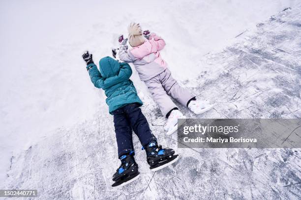 a boy and a girl in skates lie on a cat in a snowdrift. - figure skating child stock pictures, royalty-free photos & images