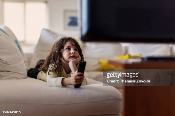 six year old boy sitting on a couch, holding a remote control, watching tv - thanasis zovoilis stock pictures, royalty-free photos & images