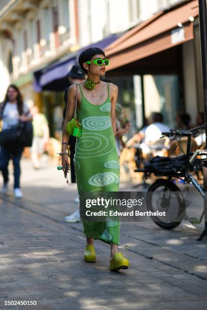 Guest wears neon green sunglasses from Versace, a black and green pearls with large green flower pattern necklace, a green with white latte...