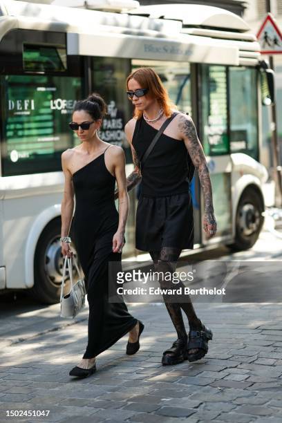 Guest wears black sunglasses, a black asymmetric shoulder top, a black long silk skirt, a white latte matte leather handbag, silver large bracelets,...