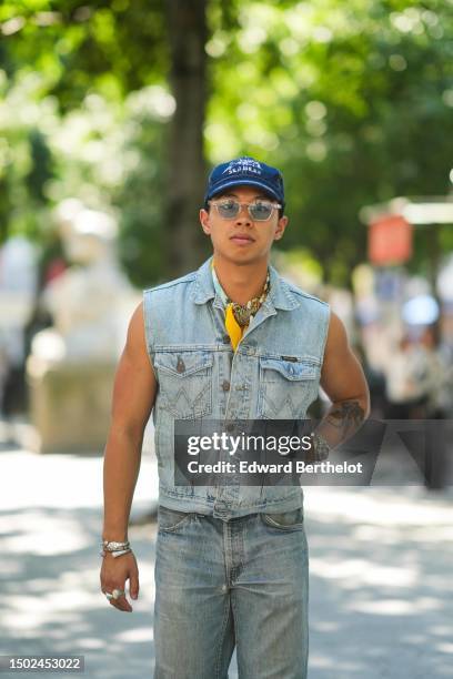 Guest wears a navy blue denim with white inscriptions pattern cap, transparent sunglasses, a pale blue / yellow / white print pattern silk scarf, a...