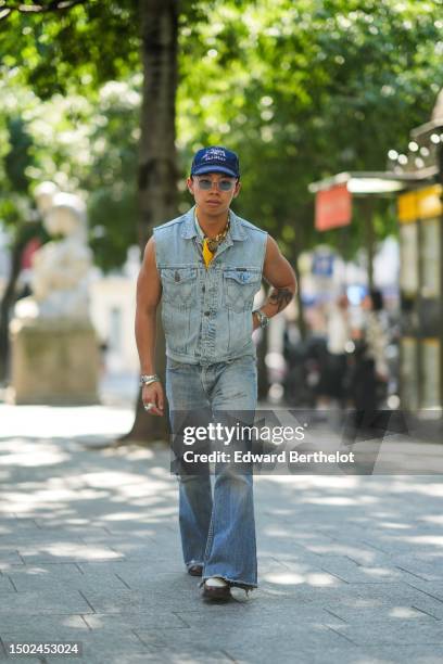 Guest wears a navy blue denim with white inscriptions pattern cap, transparent sunglasses, a pale blue / yellow / white print pattern silk scarf, a...