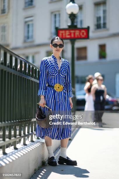 Guest wears black sunglasses, a white and navy blue striped print pattern / embossed embrodiered breastplate midi dress, a black shiny leather with a...