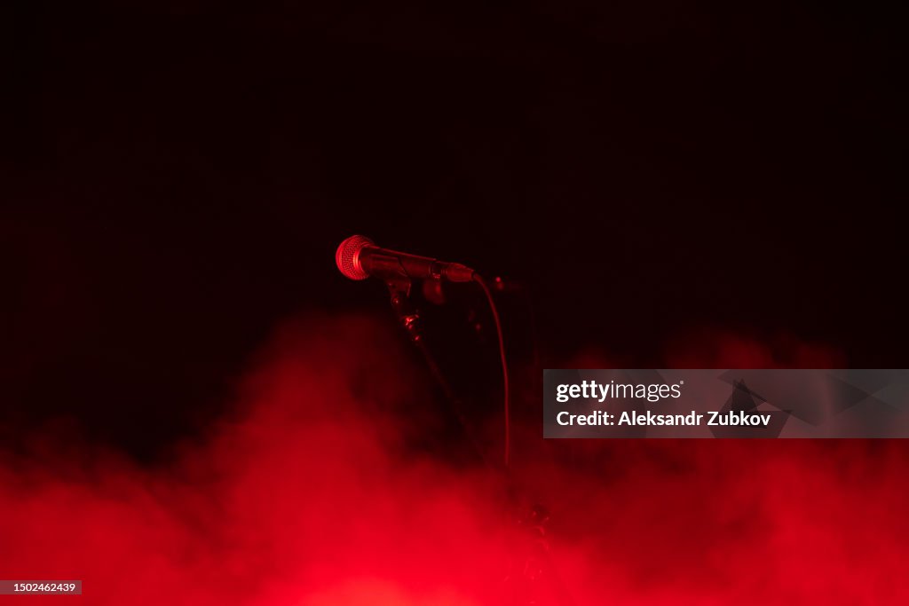 Microphone on stage, against the background of bright stage smoke. Karaoke, night club, bar. A musical concert. A scene with multicolored lights. Song, musical concept. The spotlight shines brightly through the darkness. Music and lighting equipment.