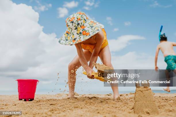 a family beach scene - a little girl builds sandcastles as a little boy wearing a snorkle runs towards the ocean - kind sandburg stock-fotos und bilder