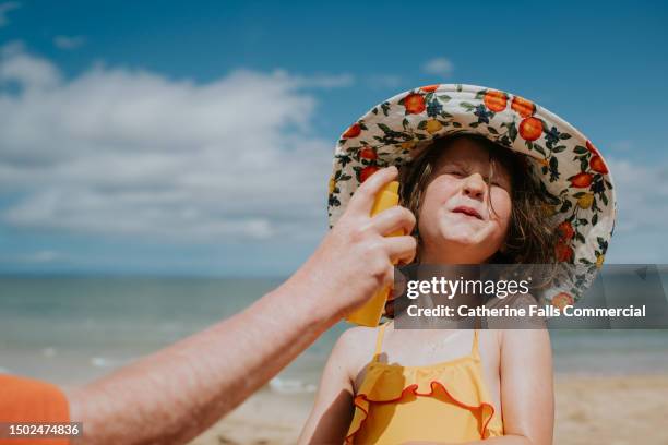 a parent applies sunscreen to a child's face - she braces as she prepares to be spritzed in the face - humour à la plage photos et images de collection