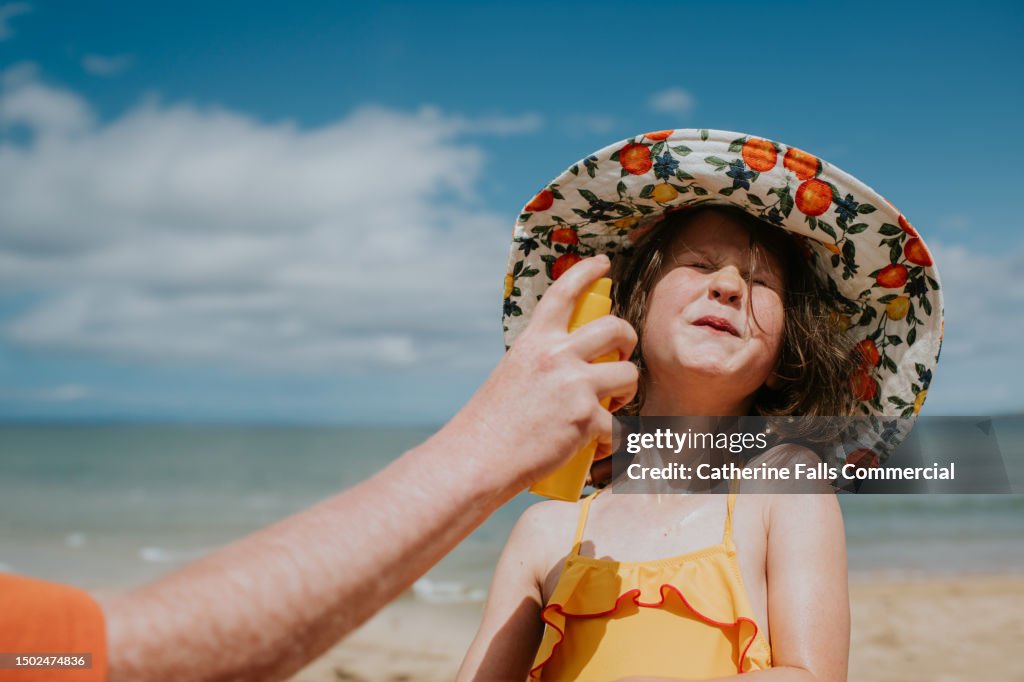 A parent applies sunscreen to a child's face - she braces as she prepares to be spritzed in the face