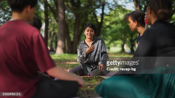 personas de grupos multiétnicos que se reúnen en la naturaleza para una sesión de terapia grupal - manos sobre el pecho fotografías e imágenes de stock
