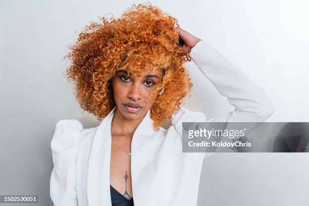 vibrant afro-latina model: elegant contrast of white jacket, orange voluminous hair, and kicked wall - teased hair stock pictures, royalty-free photos & images