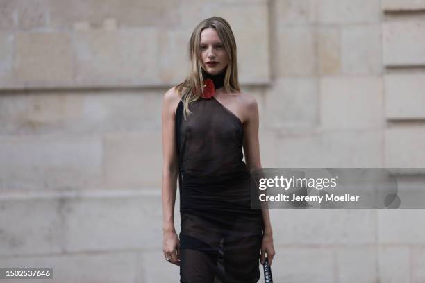 Maya Stepper is seen wearing shiny black high heels, a dark leather bag and a transparent one piece-suit with a single flamongo flower on top near...