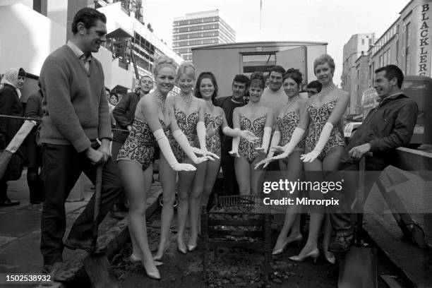 Dancers warm themselves round the blazing brazier watched by workmen during their lunch break. December 1969.