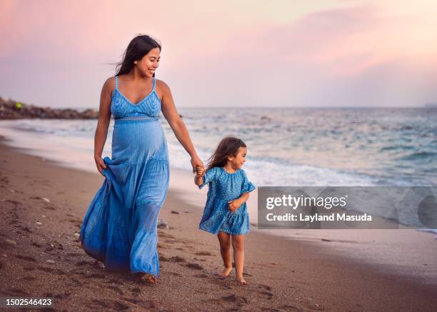 pregnant woman with young daughter on beach - girl blowing sand stock-fotos und bilder