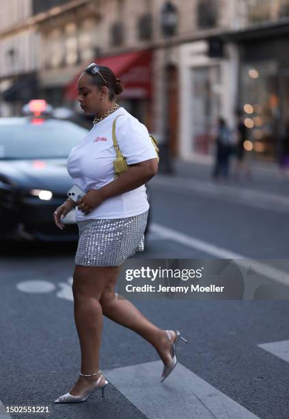 Fashion Show Guest is seen wearing miu miu shades, golden jewelry, a white tshirt with the logo of jean paul gautier, a shiny silver skirt, silver...