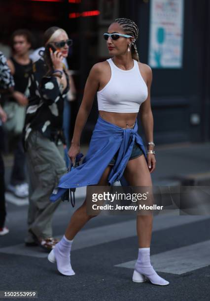 Fashion Show Guest is seen wearing light blue shades, a tank top with open belly, blue jeans-like shorts, a blue shirt bound on her waist and white...