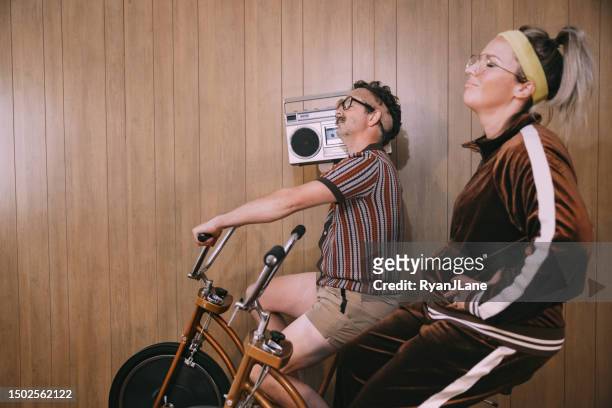 retro nineteen eighties aesthetic exercise bike couple - funky middle age couple stockfoto's en -beelden