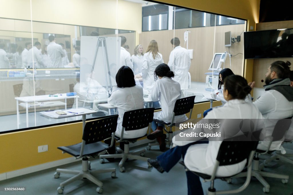 Medical students observing practical classes from outside the classroom through a glass window