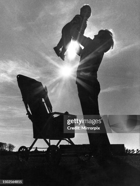 Mother swings her baby through the air during a British summer holiday. Circa 1970.