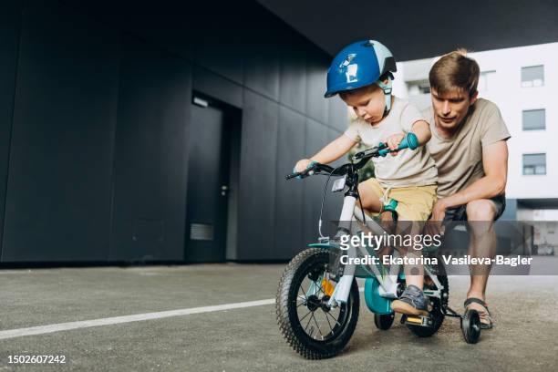 dad teaches his three-year-old son to ride a bike in the summer in the city yard - daily life in zagreb stock pictures, royalty-free photos & images