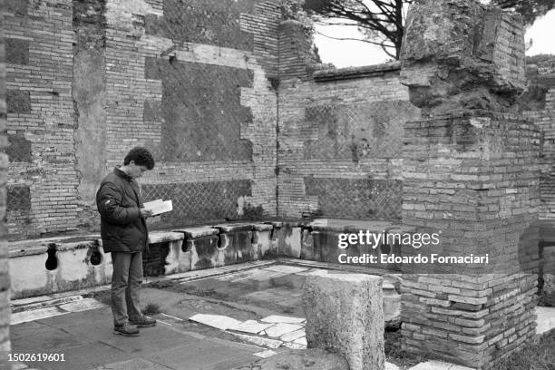 Visitors looks at a guidebook as he stands among latrines in the ruins of the ancient city of Ostia Antica, near Ostia, Italy, February 10, 1987.
