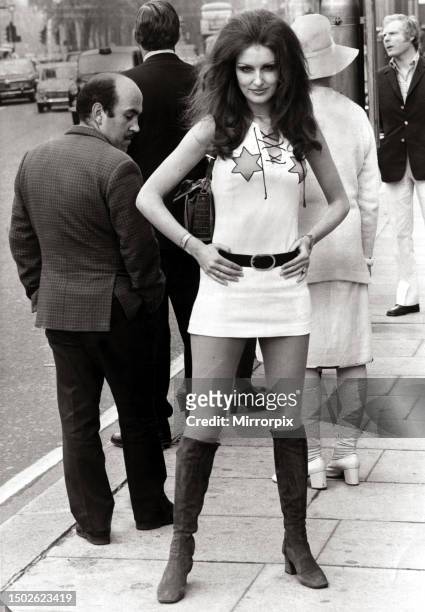 Female model Beulah Hughes wearing a mini dress and knee high boots in a London street as a man turns round to get a better view. May 1971.
