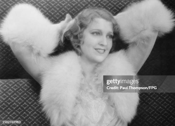 American actress and singer Jeanette MacDonald wearing a jacket trimmed with white fur, posing with her hands behind her head, United States, circa...