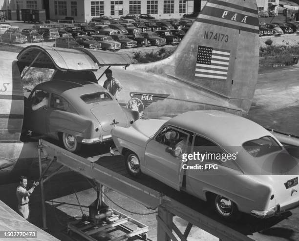 Two Kaiser-Frazer Corporation Henry J automobiles driven up a ramp to be loaded aboard a Pan-American World Airways Curtiss Wright C-46F cargo...