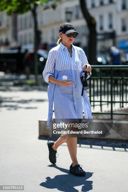 Guest wears a black denim cap from Louvre, black circle sunglasses, silver earrings, large silver chain necklaces, a white with navy blue striped...