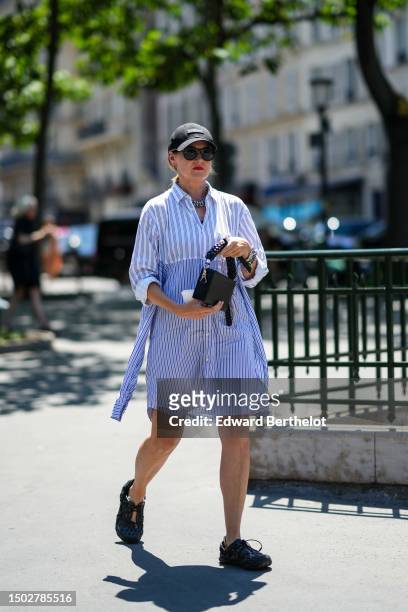 Guest wears a black denim cap from Louvre, black circle sunglasses, silver earrings, large silver chain necklaces, a white with navy blue striped...