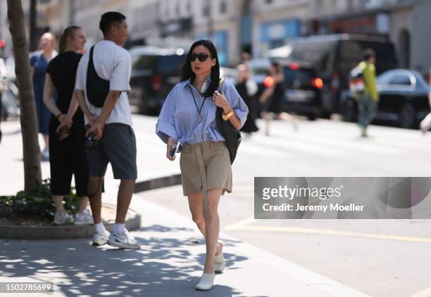 Fashion Week Guest is seen wearing black shades, a blue white and black striped shirt, a black bag with golden ornaments, a beige shorts with a long...